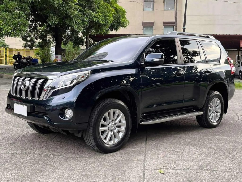 Toyota Land Cruiser Prado 4x4 rental car driving on a scenic winding road through the green terraced hills of Rwanda.