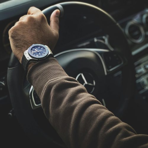 Close-up of a hand wearing a watch while holding a car steering wheel.